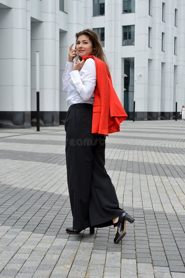 ένα κορίτσι με λευκό πουκάμισο και μαύρο παντελόνι με κόκκινο σακάκι στα  χέρια της Στοκ Εικόνα - εικόνα από workplace: 192814815