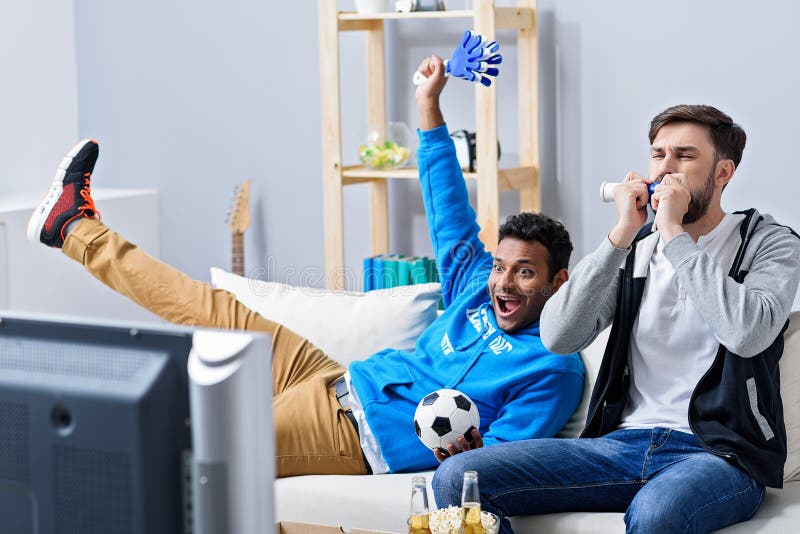 Звезды смотрят футбол. Спорт по телевизору. Болельщик смотрит футбол с мобильным телефоном. Парни смотрят футбол в гостиной. Мужчина смотрит футбол.