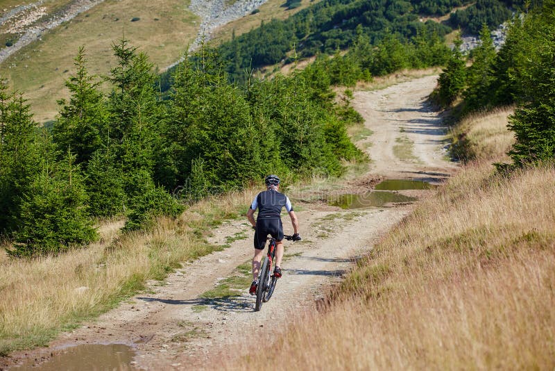 Велосипедист едет в гору. Грунтовая дорога для велосипедистов в горах. Велосипедист уезжает в горы. Велосипедист по грунтовой дороге к озеру.