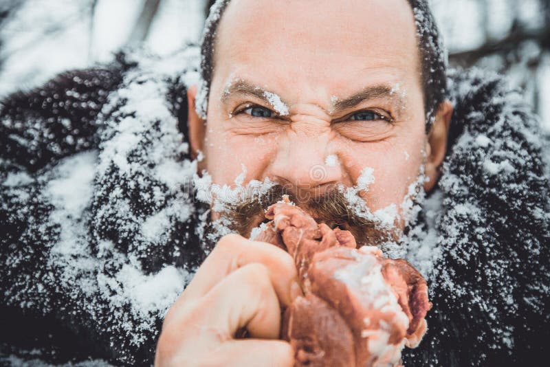 Снег голодный. Бородатый мужик ест мясо. Мужчина ест сырое мясо.