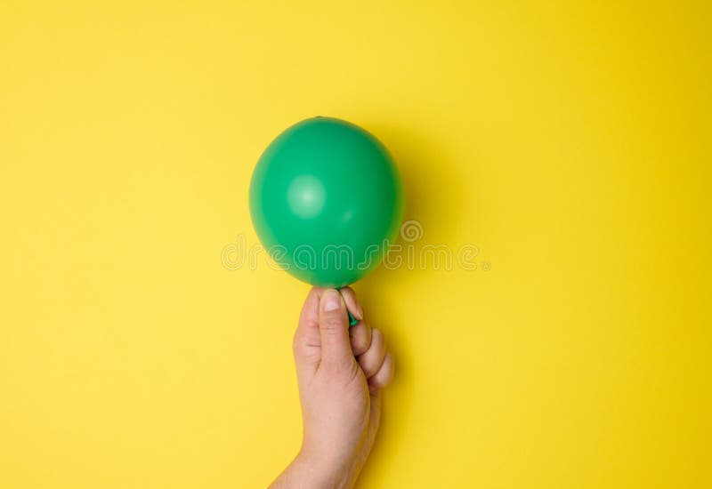 Надуваем зеленые воздушные шарики. Надутый зеленый шарик держит в руках.