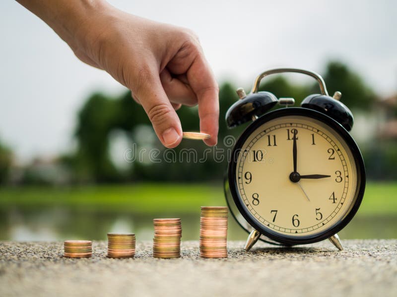  Закройте вверх по руке кладя деньги к стогу монеток с временем, концепцией стоимости денег времени в теме финансов дела Деньги сб стоковое изображение rf