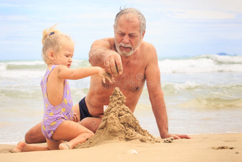  Замок песка строения мальчика девушки Grandpa маленький белокурый на пляже стоковые фото