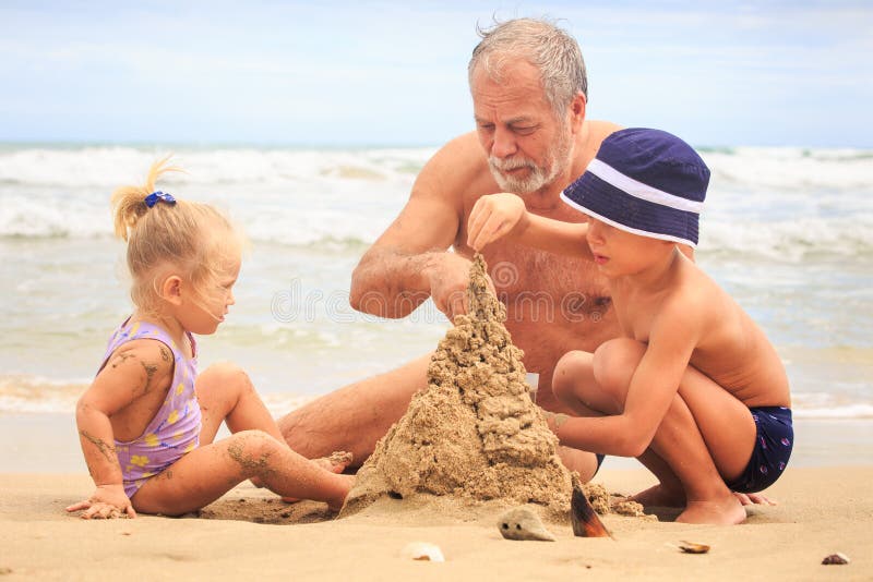  Замок песка строения мальчика девушки Grandpa маленький белокурый на пляже стоковая фотография rf