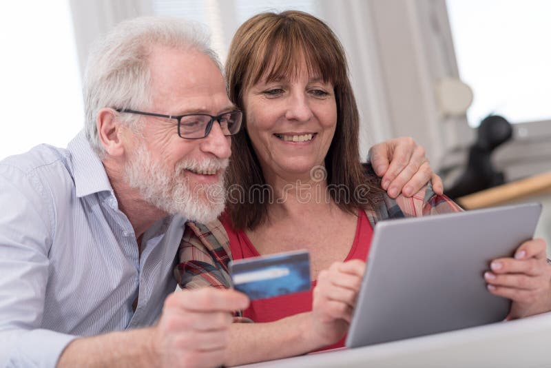 Mature Couple Relaxing, Using Laptop And Digital Tablet In Bedroom