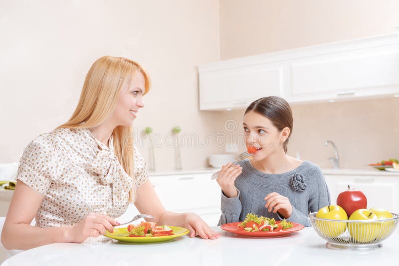 Мама имеет дочь. Мама и дочка обедают. Мама с дочкой обедают за столом. Мама и дочка сидят за столом с едой. Мать с дочерьми обедает.