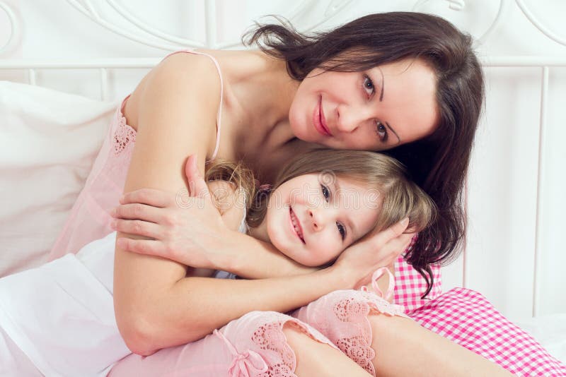 Мать и дочь обнимаются постель. Мама с дочкой обнимаются на кровати. Мама с дочкой фотосессия на кровати.