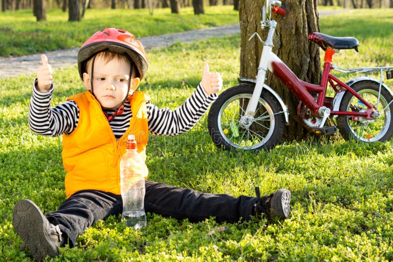 Мальчик сидит на велосипеде. Маленький мальчик катается. Маленький мальчик в велошлеме. Дети на велосипеде весёлые палецм вверх.