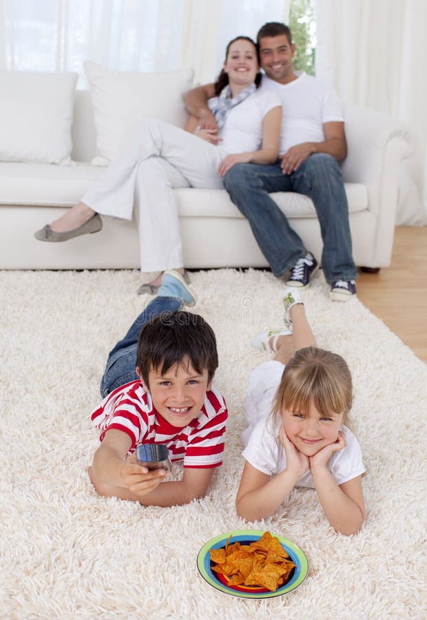 Непослушные брат и сестра. Семья лежит на полу. Семья лежит на теплом полу. Брат с сестрой смотрят телевизор. Брат и сестра смотрят ТВ.