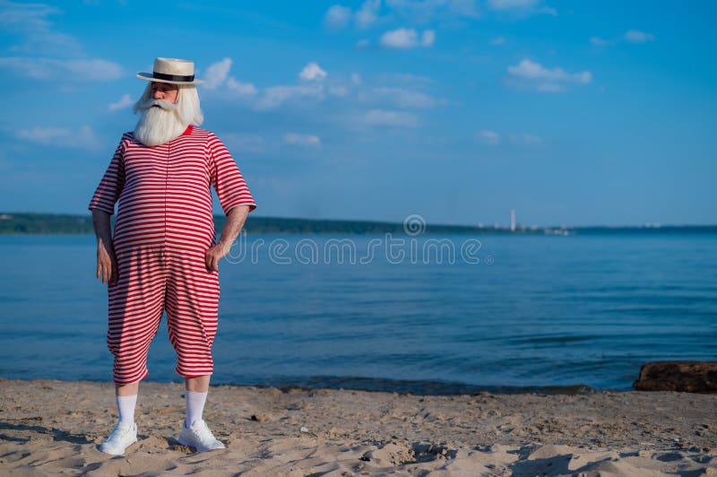 пожилой мужчина в полосатом ретро-купальнике и лодке на берегу моря  Стоковое Фото - изображение насчитывающей трусливый, затишье: 222296016