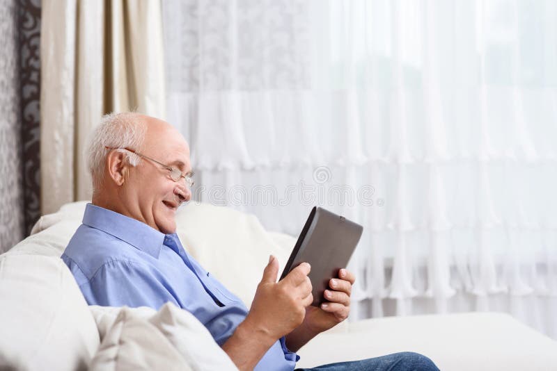 В скромно обставленном кабинете сидел пожилой человек. Старик сидит на диване. Старик сидит на диване и улыбаются. Дед держит планшет. Обшарпанное помещение седовласый старик сидит за компьютером.