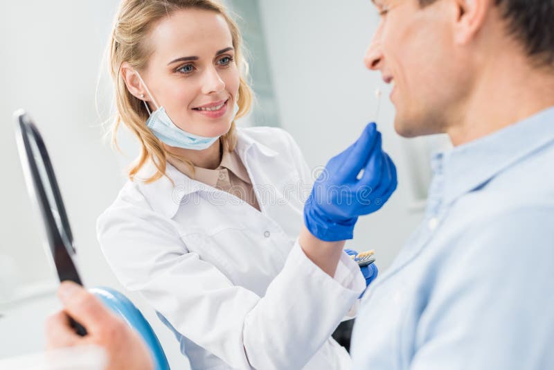 Больной подобрать. Woman choosing Tooth Implant looking at Mirror in Modern Dental Clinic.