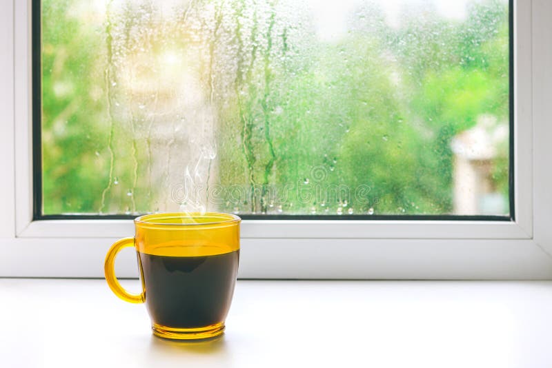Чашка горячего кофе на windowsill Вне окна дождь
