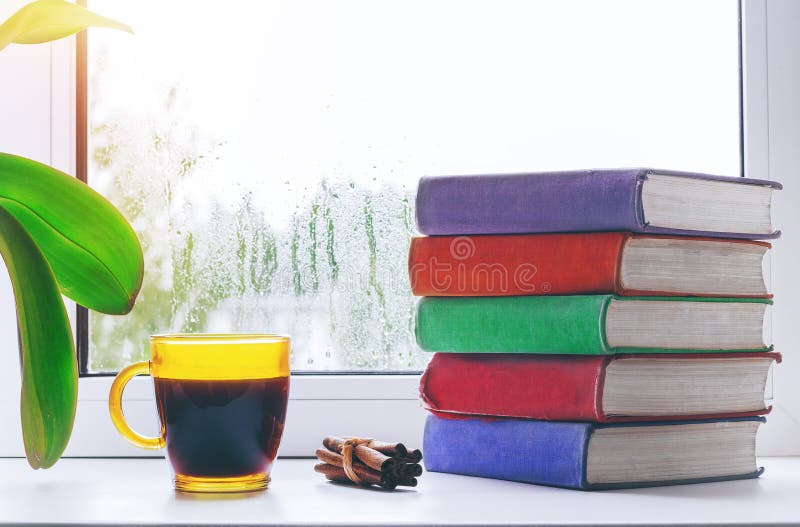 Чашка горячего кофе с циннамоном и стог книг на windowsill Вне окна дождь конструированный тип комнаты домашнего интерьера живя р