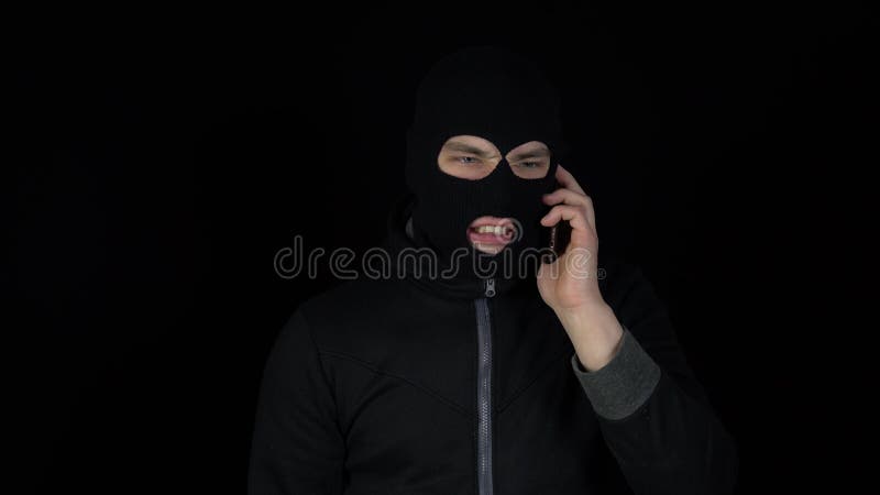 Человек в маске балаклавы говорит по телефону. Бандит кричит по телефону на  черном фоне. Стоковое Фото - изображение насчитывающей рэкетер, шантажист:  215064290