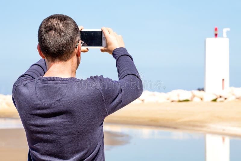 Мобильный девайс которым снимают селфи. Парень фотографирует на телефон. Человек спиной к камере. Человек фоткает спиной.