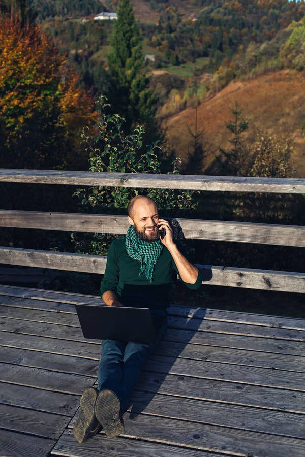 自由职业者胡须男 坐在山上的平台上 手提电脑 在电话里聊天库存图片 图片包括有网络 生活方式