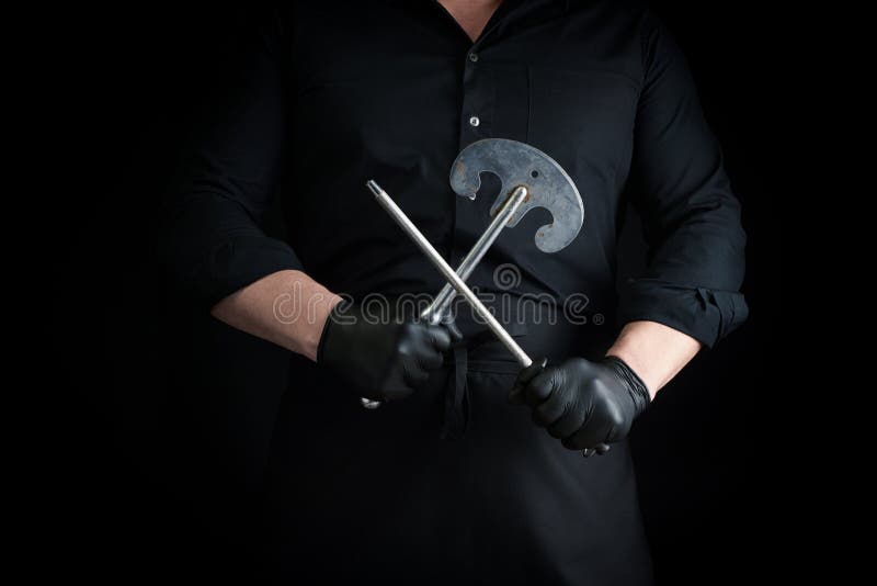 黑色制服和黑色胶乳手套的男厨拿着一把大尖尖的古刀 用于肉类和蔬菜 还有一把金属剃须刀库存图片 黑色制服和黑色胶乳手套的男厨拿着一把大尖尖的古刀 用于肉类和蔬菜 还有一把金属剃须刀库存图片