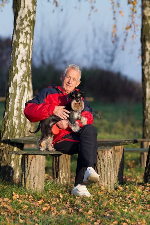 Älterer Mann, Der Auf Einer Bank Mit Seinem Hund In Einem Park Sitzt