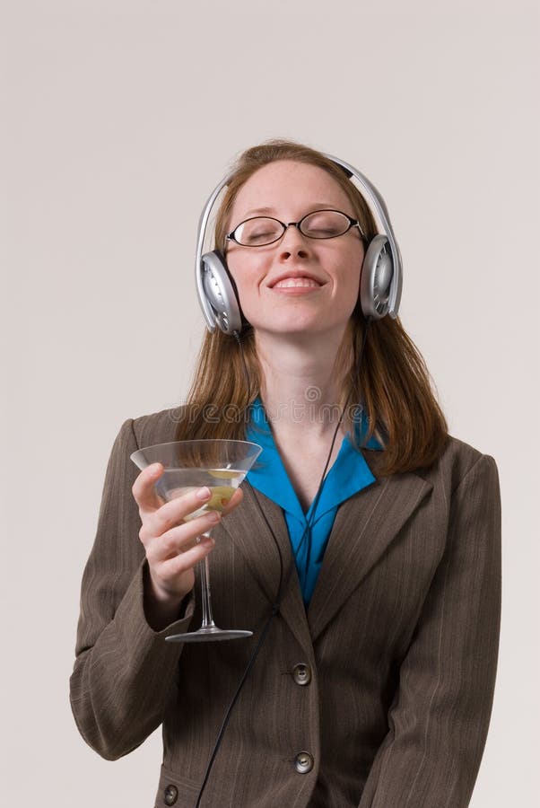 A young business woman relaxes with a martini and music after work. A young business woman relaxes with a martini and music after work