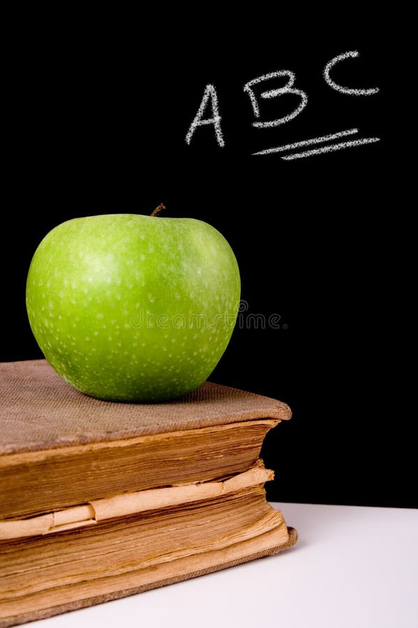 Green apple on top of a very old book. Chalkboard with ?ABC? letters on it as background. Green apple on top of a very old book. Chalkboard with ?ABC? letters on it as background