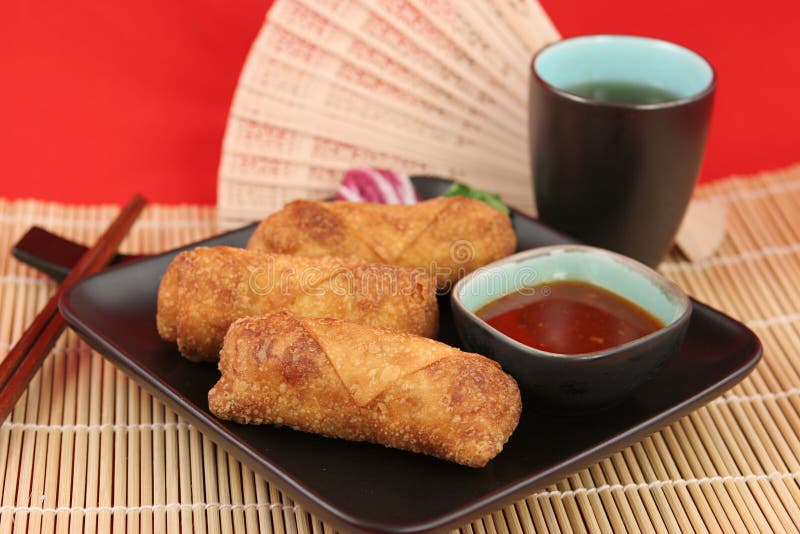 Crispy fried egg rolls with dipping sauce, served on a bamboo mat with tea. Crispy fried egg rolls with dipping sauce, served on a bamboo mat with tea.