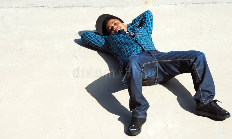 A skater takes a break on a cement ramp, casting an interesting shadow on the ground. A skater takes a break on a cement ramp, casting an interesting shadow on the ground.