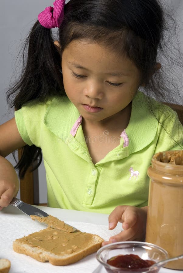 A young child makes a peanut butter and Jelly sandwich. A young child makes a peanut butter and Jelly sandwich