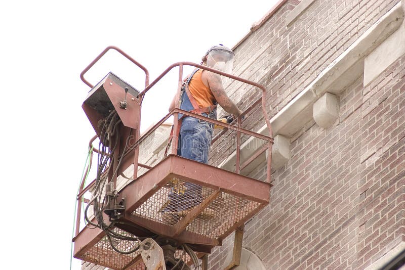 A construction worker grinding out old motar around bricks on a local church. A construction worker grinding out old motar around bricks on a local church