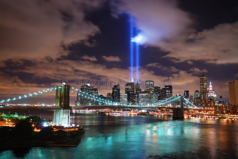 Remember September 11. New York City Manhattan panorama view with Brooklyn Bridge at night with office building skyscrapers skyline illuminated over Hudson River and two light beam in memory of September 11. Remember September 11. New York City Manhattan panorama view with Brooklyn Bridge at night with office building skyscrapers skyline illuminated over Hudson River and two light beam in memory of September 11.