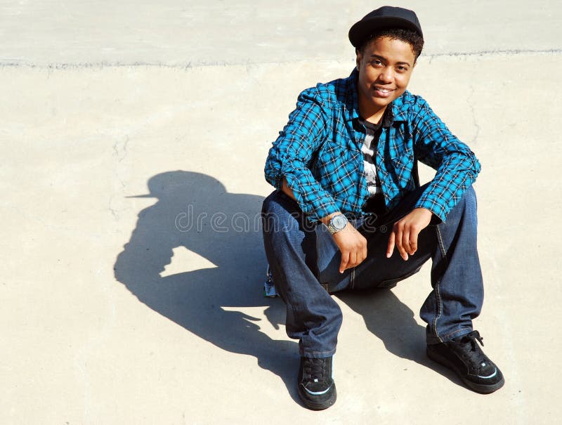 A skater takes a break on a cement ramp, casting an interesting shadow on the ground. A skater takes a break on a cement ramp, casting an interesting shadow on the ground.