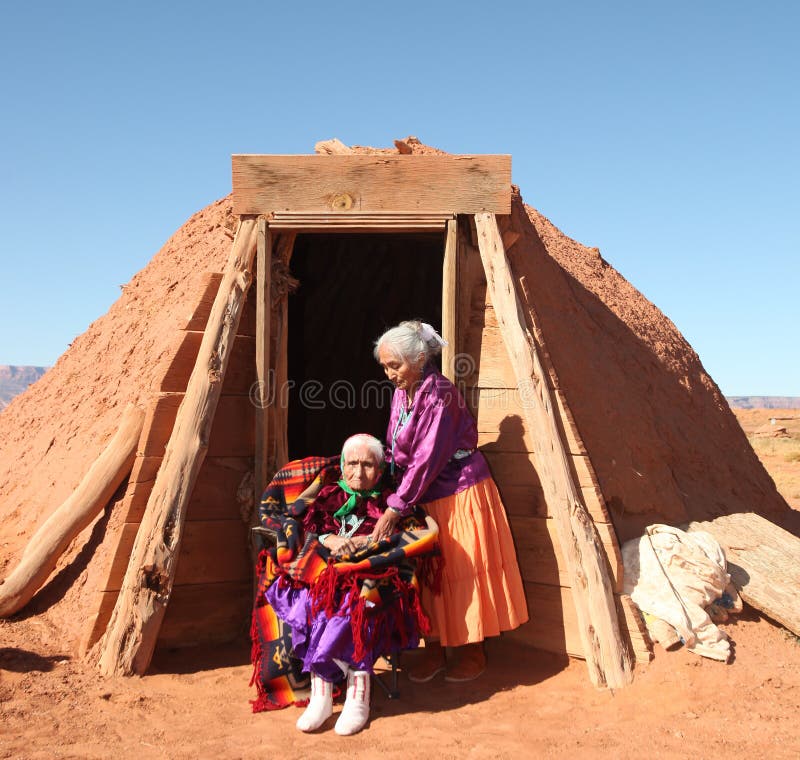 2 mulheres do Navajo fora de sua cabana tradicional de Hogan
