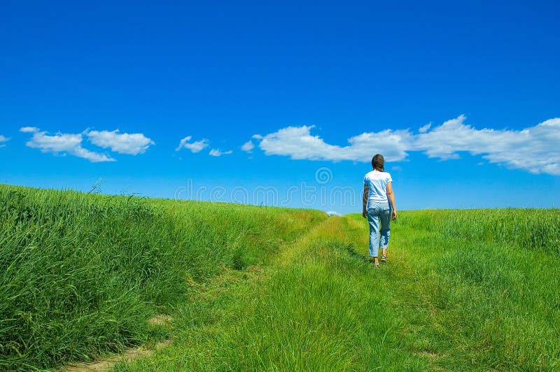 Person walking through bright green field under blue sky with clouds. Person walking through bright green field under blue sky with clouds