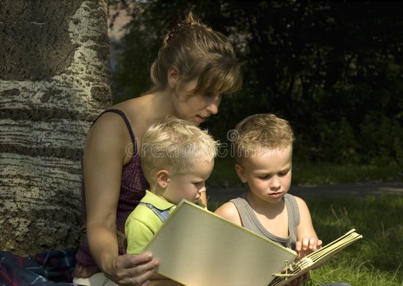 Family reading a book while sitting against a tree. Family reading a book while sitting against a tree