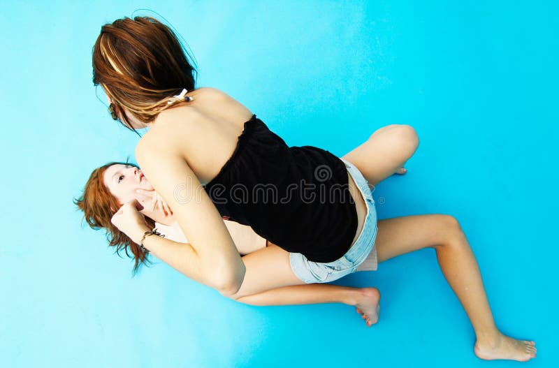 Two teenage girls wrestling on the floor. One girl is sitting on top of the other. Two teenage girls wrestling on the floor. One girl is sitting on top of the other.