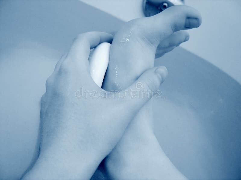 Hand holding white soap, cleaning bottom of feet in bathtub. Hand holding white soap, cleaning bottom of feet in bathtub.