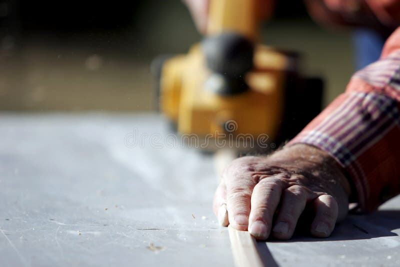 Close-up of a construction worker's hand and power tool while planing a piece of wood trim for a project (shallow focus). Close-up of a construction worker's hand and power tool while planing a piece of wood trim for a project (shallow focus).