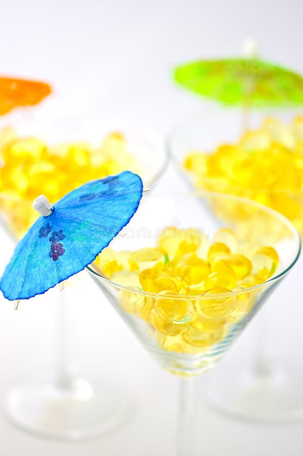 Three martini glasses filled with cod liver oil capsules, sources of vitamin a, vitamin d and omega-3, decorated with mini parasols, isolated on white. Three martini glasses filled with cod liver oil capsules, sources of vitamin a, vitamin d and omega-3, decorated with mini parasols, isolated on white