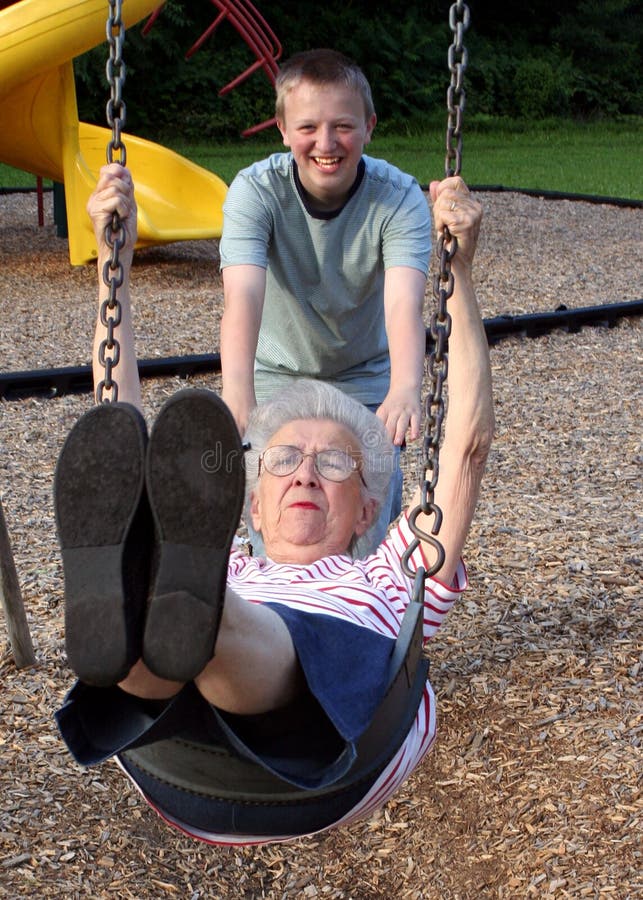 Teenage grandson pushing his grandmother on a playground swing. Teenage grandson pushing his grandmother on a playground swing.