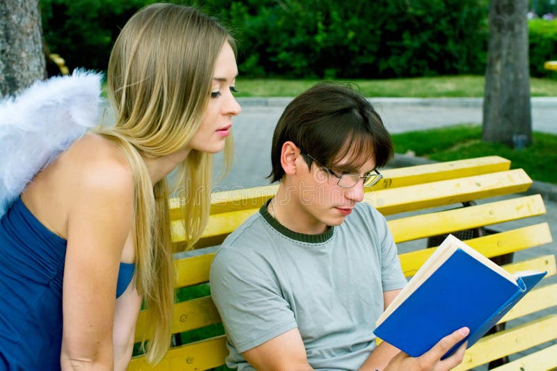 A young men reading a book in a summer park. Guardian Angel is sitting next to him. A young men reading a book in a summer park. Guardian Angel is sitting next to him