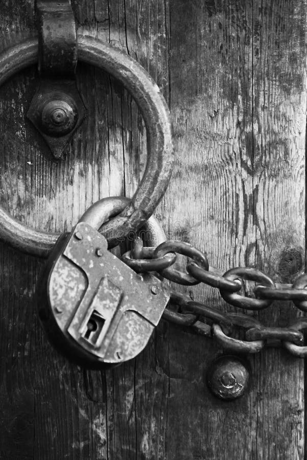 Heavy wooden doors with chains and padlocks are all about security. Closeup shot of a heavy padlock with chains on a castle portal. Shallow depth of field with focus mainly on chain and wooden door. Heavy wooden doors with chains and padlocks are all about security. Closeup shot of a heavy padlock with chains on a castle portal. Shallow depth of field with focus mainly on chain and wooden door