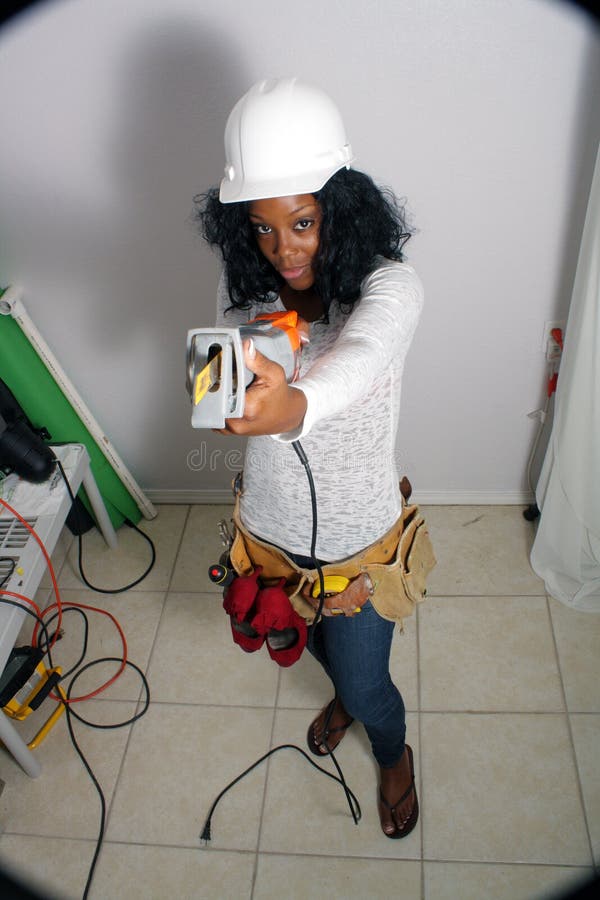 An extraordinarily beautiful young black woman wearing a tool belt that holds her dress shoes, points her reciprocating saw at the camera. Wide angle, high POV, with slight vignetting at the corners for effect. An extraordinarily beautiful young black woman wearing a tool belt that holds her dress shoes, points her reciprocating saw at the camera. Wide angle, high POV, with slight vignetting at the corners for effect.