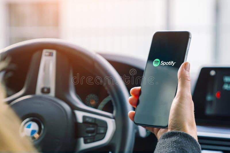 Woman holding a Apple iPhone opening Spotify Music streaming app in a car. Streaming music via the