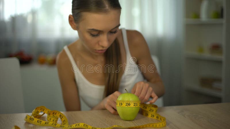 Aan anorexie lijdend meisje die appel met band meten, die calorieën en de index van de lichaamsmassa tellen
