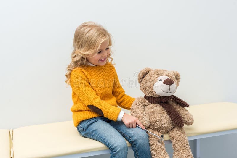 aanbiddelijk meisje die neurologieonderzoek van teddybeer doen terwijl het zitten stock foto's aanbiddelijk meisje die neurologieonderzoek van teddybeer doen terwijl het zitten stock foto's