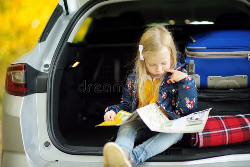 Adorable girl with a suitcase ready to go on vacations with her parents. Child looking forward for a road trip or travel. Autumn break at school. Traveling by car with kids. Adorable girl with a suitcase ready to go on vacations with her parents. Child looking forward for a road trip or travel. Autumn break at school. Traveling by car with kids.