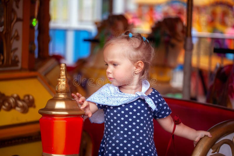 Aanbiddelijk meisje in stipkleding dichtbij het carrouselpaard in openlucht in de zomerdag royalty-vrije stock foto Aanbiddelijk meisje in stipkleding dichtbij het carrouselpaard in openlucht in de zomerdag royalty-vrije stock foto