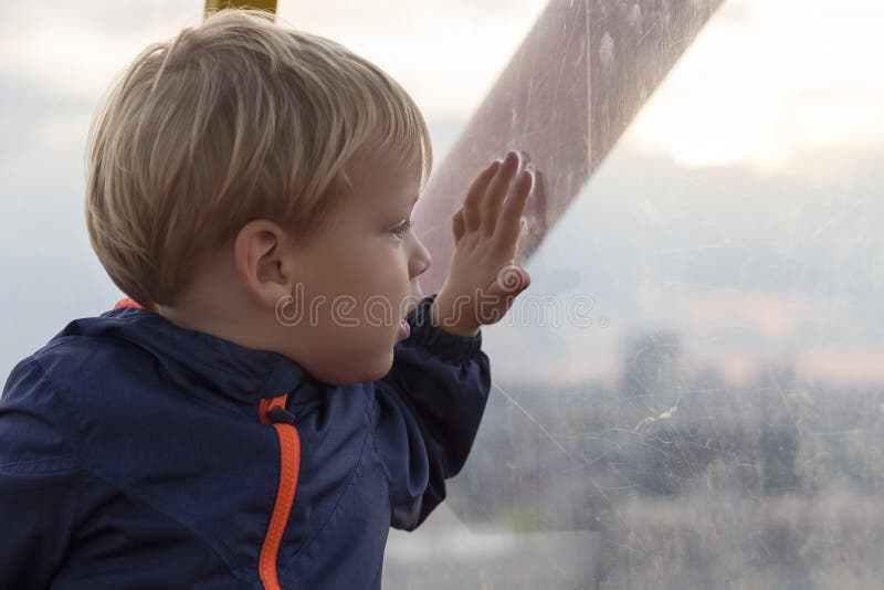 Aanbiddelijk weinig blonde zitting van de jong geitjejongen dichtbij venster en buiten het kijken stock fotografie Aanbiddelijk weinig blonde zitting van de jong geitjejongen dichtbij venster en buiten het kijken stock fotografie