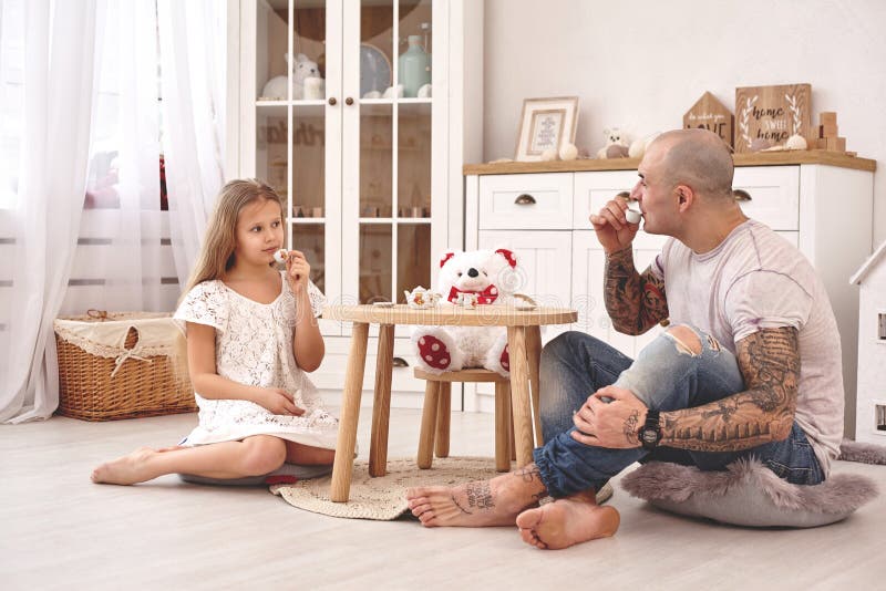 Aanbiddelijke dochter die een witte kleding dragen whith haar houdende van vader Zij drinken thee van een stuk speelgoed schotels stock afbeelding Aanbiddelijke dochter die een witte kleding dragen whith haar houdende van vader Zij drinken thee van een stuk speelgoed schotels stock afbeelding