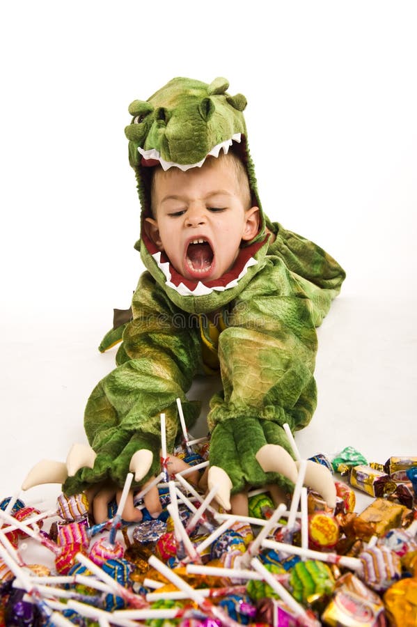 Adorable boy in a crocodile costume playing trick or treat and digging into a huge pile of candy during Halloween. Adorable boy in a crocodile costume playing trick or treat and digging into a huge pile of candy during Halloween.